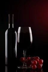 Fotobehang Bottle of red wine, a glass of red wine and grapes on a dark background. © Anna