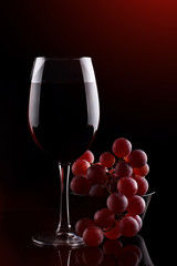 A glass of red wine and red grapes on a dark background.