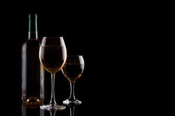 A bottle of white wine and two glasses with white wine on a dark background.