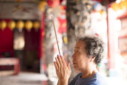 senior woman praying buddha with incense stick at temple