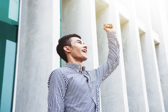 Asian Young and Happiness Businessman in Raised arms in Cheerful posture to Celebrate his Life at outside office building, Successful and business achievement concept