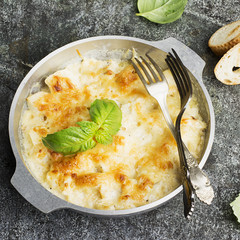 Fragrant homemade casserole with cod and onion in cream sauce with horseradish under a cheese ruddy crust in a form on a gray background with crispy grilled toast. Top View.