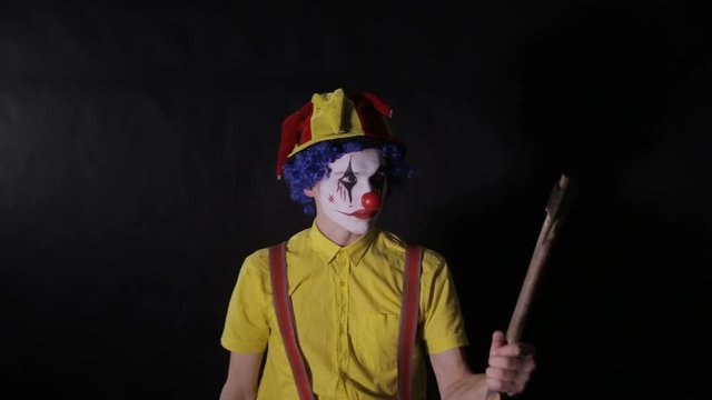 A crazy clown imitates a blow of an axe. 