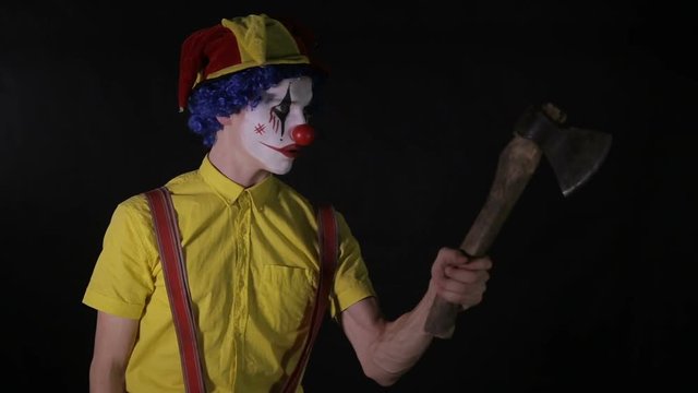 A clown juggles a wooden axe with one hand. 
