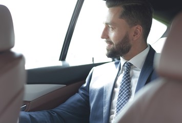 Smiling business man sitting in the back seat of a car