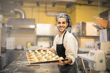 Young cheerful pastry chef holding a croissant's tray