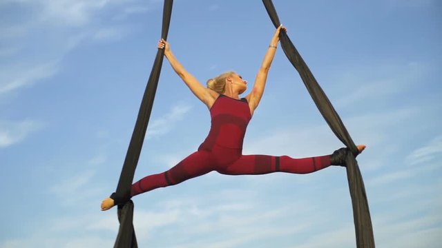 Youngl woman dancing with aerial silk on a sky background rapid slow motion