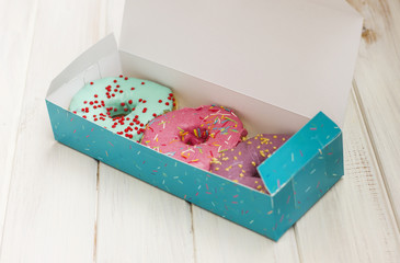 Colorful donuts in box on the white wooden background