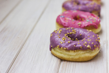 Fresh donuts with colorful glaze on the white wooden background