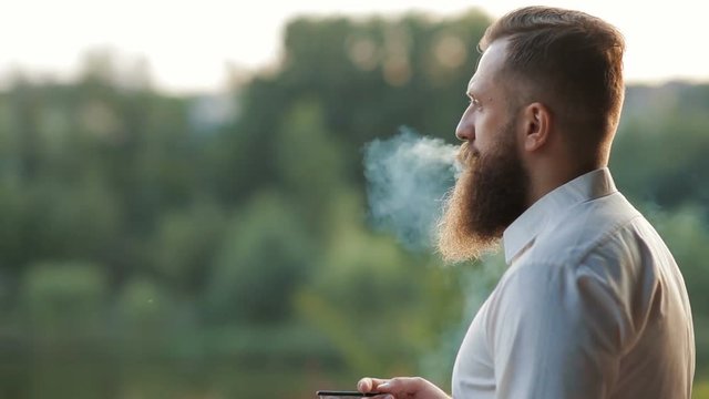 Handsome bearded man, stylish hipster male smoking cigarette outdoor