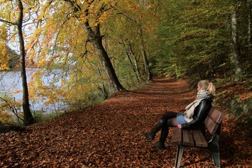 Frau sitzt auf einer Bank im Wald am malerischen Ukleisee im Herbst