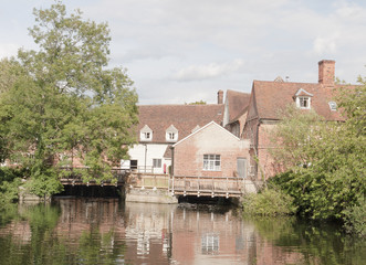 Fototapeta na wymiar Mill house at flatford mill in suffolk with river water in front and reflections, as well as trees