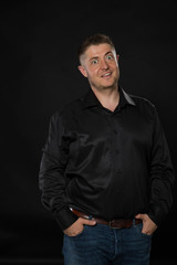 Obraz premium Young surprised man portrait of a confident businessman showing by hands on a black background. Ideal for banners, registration forms, presentation, landings, presenting concept.