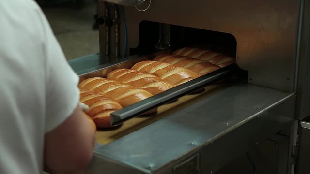 Freshly baked bread enters the conveyor from the furnace to the packaging. A bakery employee sorts the bread and slice it into a slice. Machine for cutting bread. Bread Slice Automatic Machine.