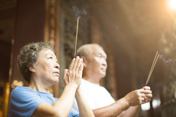 senior couple praying buddha with incense stick at temple