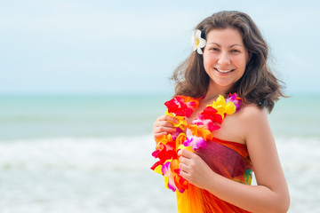 Happy young brunette in pareo and flower lei against the sea