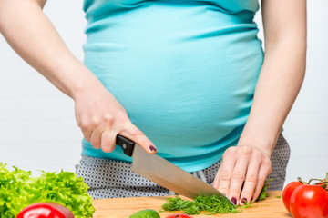 pregnant woman slices fresh herbs on a cutting board, hands close-up