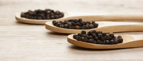 Black pepper in wooden spoon on the old board