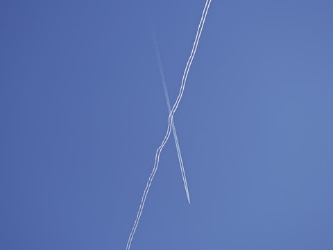 Wobbly airplane contrail crossing a straight one on deep blue sky.