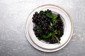 Chokeberry in silver metal bowl on grey background. Aronia berry with leaf. Top view. Copy space.