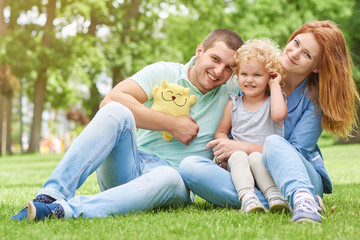 Fototapeta premium Shot of a happy young family sitting on the grass at the park together smiling to the camera copyspace lifestyle leisure weekend holidays love parenting parents children kids emotions. 