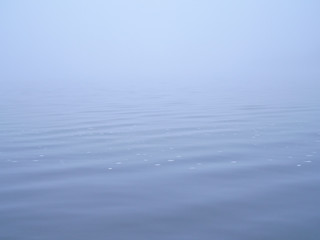 Peaceful surface of sea covered by thick white mist.