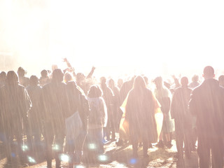 Devoted fans enjoying the concert in heavy rain. Bright lights on the stage. Music event background.