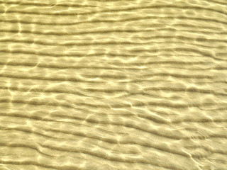 Beautiful sunlit wave pattern on the sandy sea bottom. Natural background.