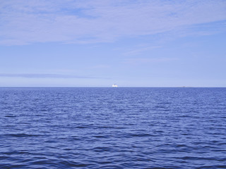 White ship sailing to the horizon on calm blue sea.