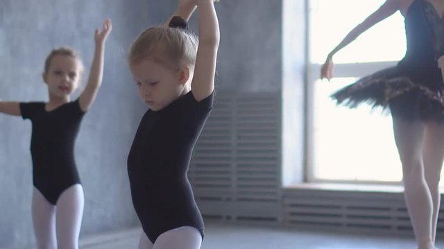 Sweet girl learning to dance in the ballet school. Little Ballerina in training in black dancing suit. Children's ballet school.
