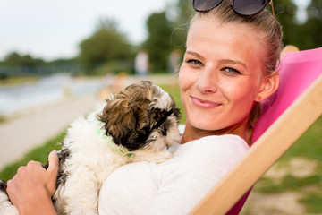 young woman holding a puppy on a sun lounger
