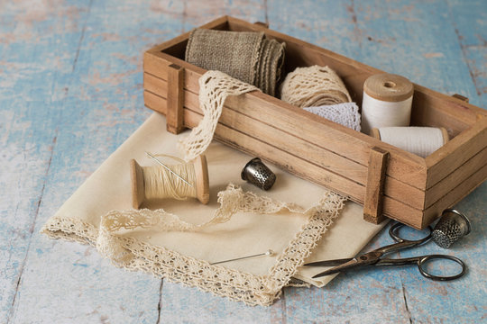   Hobby needlework.  Openwork ribbon, cloth for handkerchiefs, wooden box with sewing accessories, spools with threads, needles, scissors and thimbles on the old table.