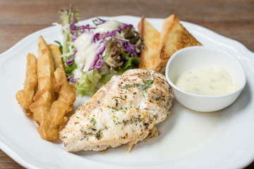 Grilled chicken breasts steak in a dish serve with vegetables and French fries on wood table in restaurant. Close up at chicken breasts steak.