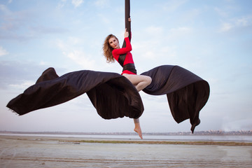 Fit woman in skinny skinny clothes dancing with aerial silk on a sky background, gymnast training...