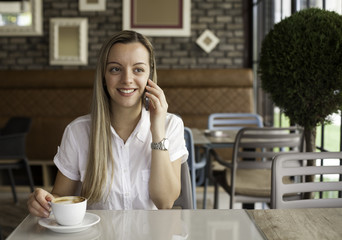 Beautiful young woman using phone in urban cafe
