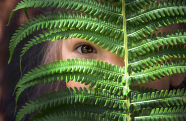 The girl looks through a gap in the fern leaf
