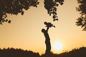Father and little baby silhouettes play at sunset
