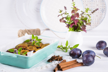 Healthy homemade dessert. Sliced red plums ready for cooking in a baking dish with fresh mint, cinnamon, anise 