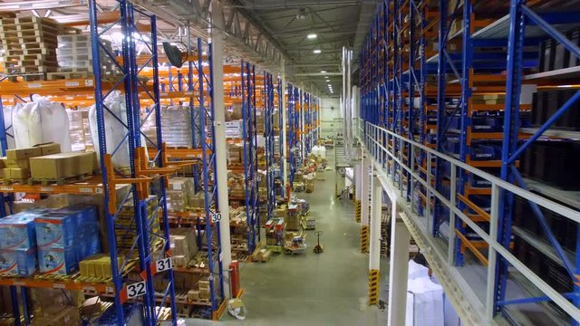 Camera goes between warehouse shelves in a modern storehouse with many racks, shelves. Aerial.
