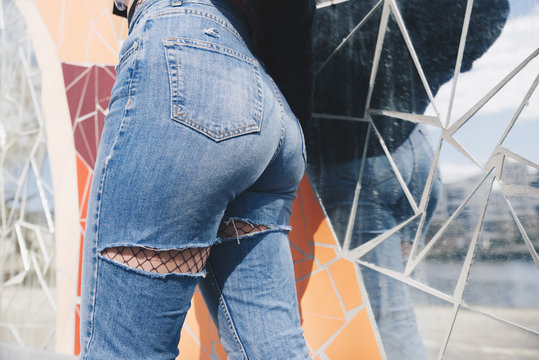 Midsection of young woman wearing torn jeans against mosaic wallMidsection of young woman wearing torn jeans against mos