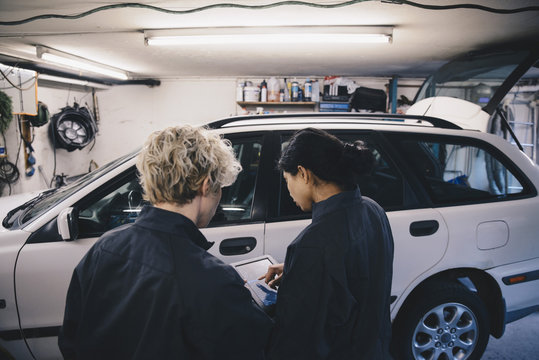 Female mechanic explaining coworker over digital tablet in auto repair shop