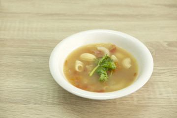 TOMATO AND MACARONI SOUP
Clear tomato and macaroni soup in a white bowl decorated with green coriander. 