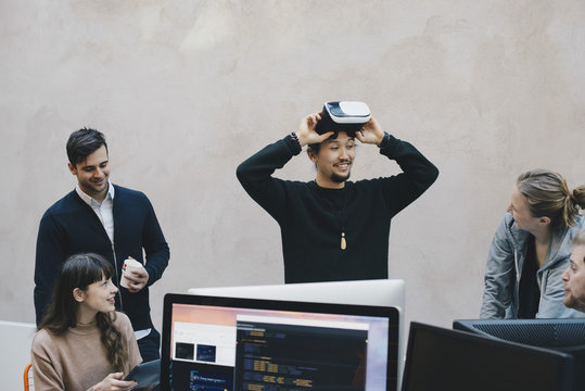 Male computer programmer wearing VR glasses while looking at colleagues in office