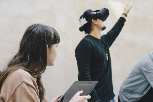 Male computer programmer gesturing while using VR glasses by colleagues in office
