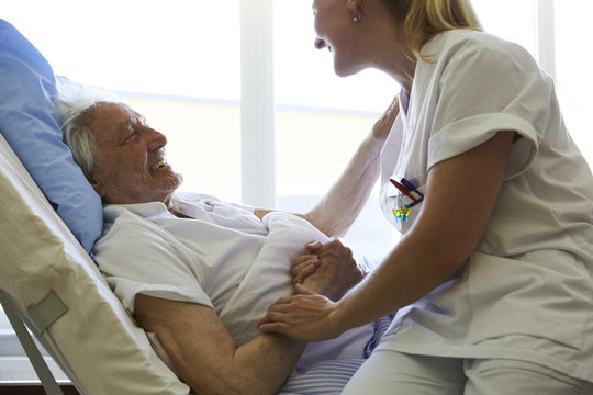 Side view of happy senior man talking to female nurse on hospital bed