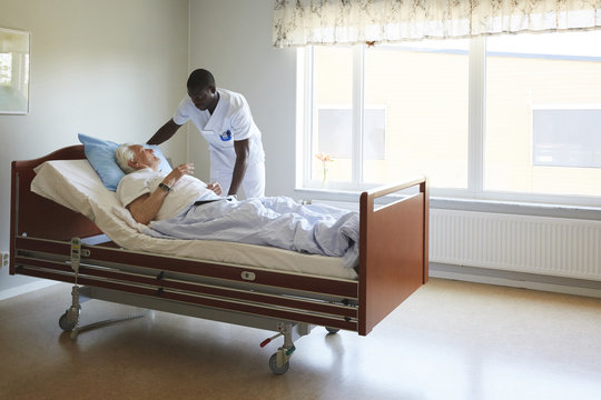 Nurse adjusting senior man's bed in hospital ward