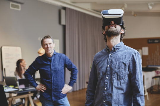 Businessman using virtual reality simulator in office with colleagues in background