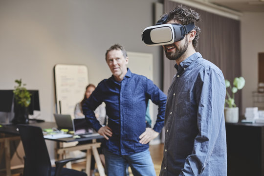 Businessman looking at colleague using virtual reality simulator in office