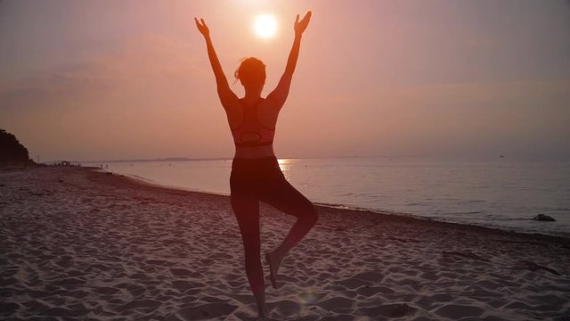 Female silhouette practicing yoga at sunrise with hands raised to the sun