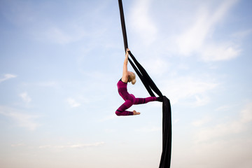 exercises with aerial silk outdoor, sky background. beautiful fit woman training acrobatic in airt.  © serejkakovalev